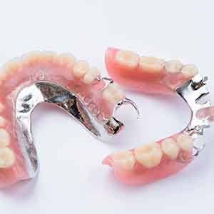 Set of partial dentures with metallic clasps on white surface