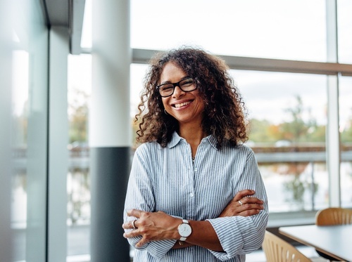 a smiling woman with glasses standing with her arms crossed