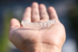 A hand holding a single Invisalign aligner